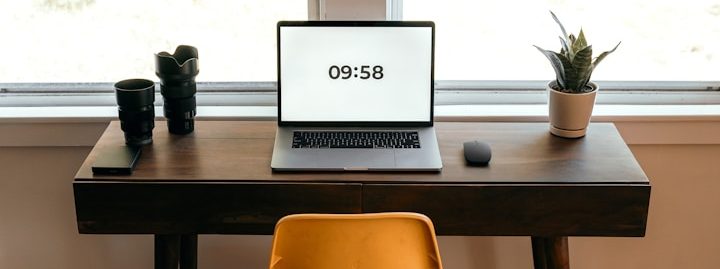 Ein Schreibtisch mit Laptop, Kaffeetassen und einer Pflanze vor einem Fenster.